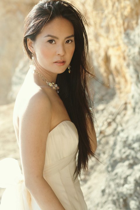 an asian girl in white gown stands on rocky beach