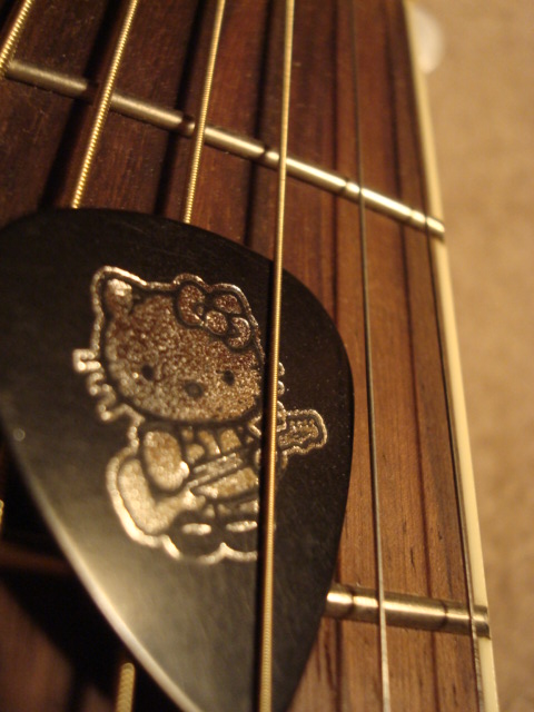 a hello kitty guitar pick sits on top of the neck of an electric guitar