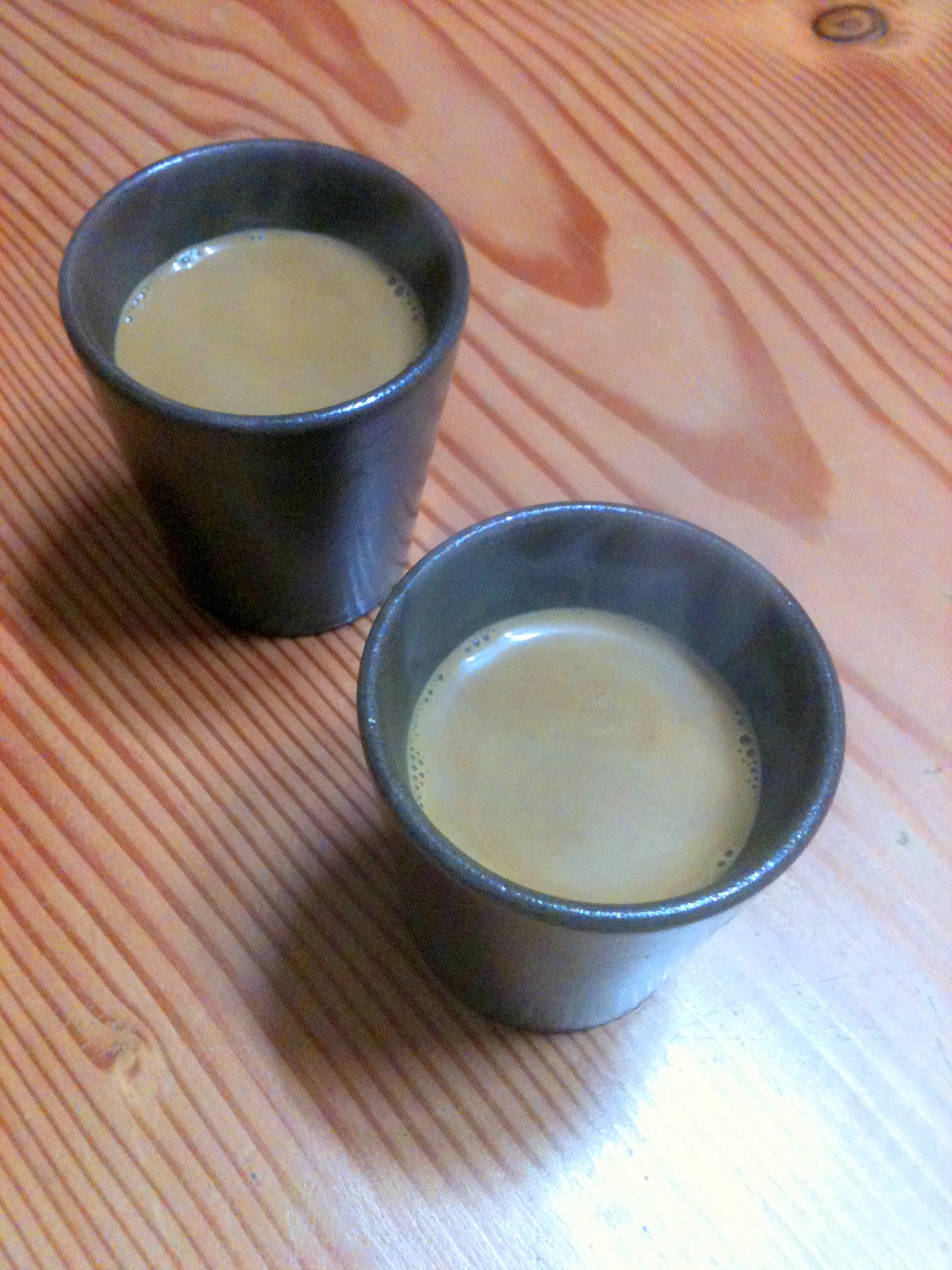 two cups sit on a table, one has a drink in it
