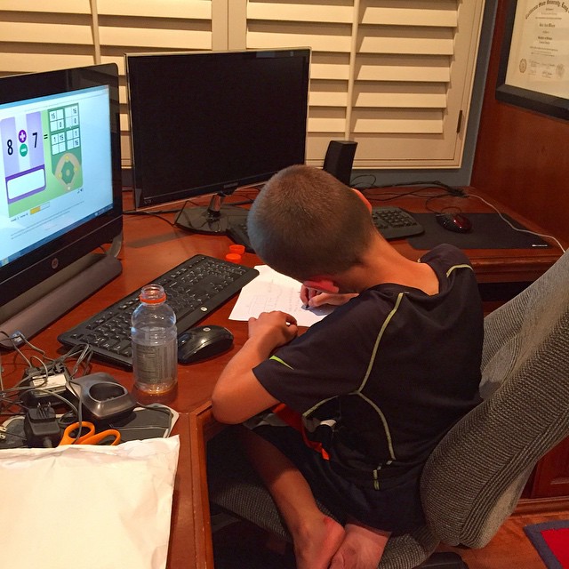 a boy sitting at a computer desk with various devices on it