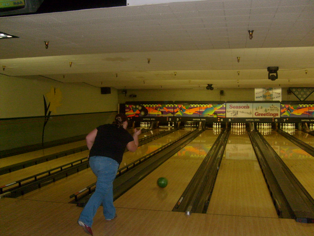 a man stands in a bowling alley holding two bowls with two legs facing down as they run towards the lanes