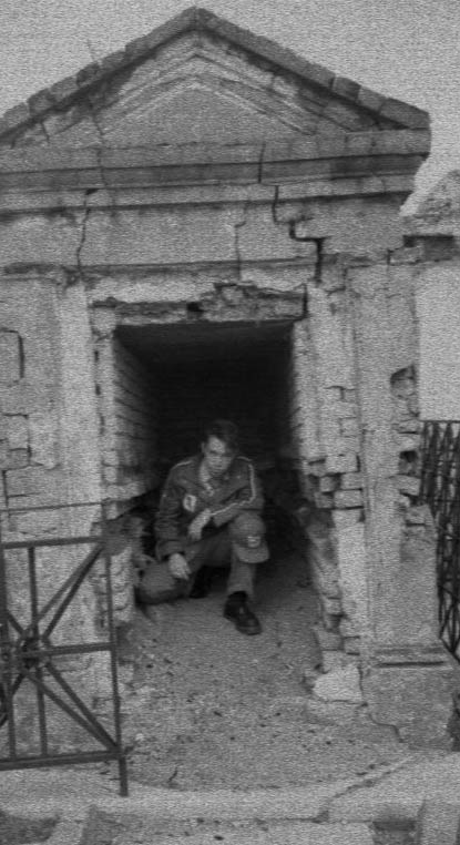 black and white image of man sitting in front of a brick doorway