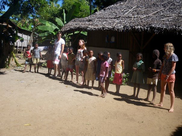 a line of s walking in front of a straw hut