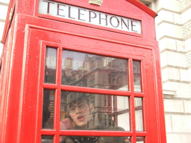 a red telephone booth in the city with a man in it