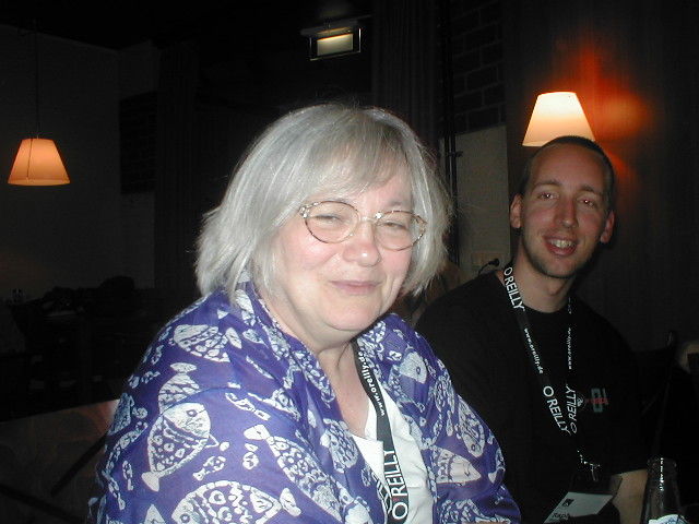 a older woman smiles at the camera as another man looks on
