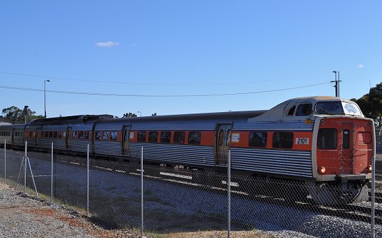 an orange and silver passenger train next to a chain link fence