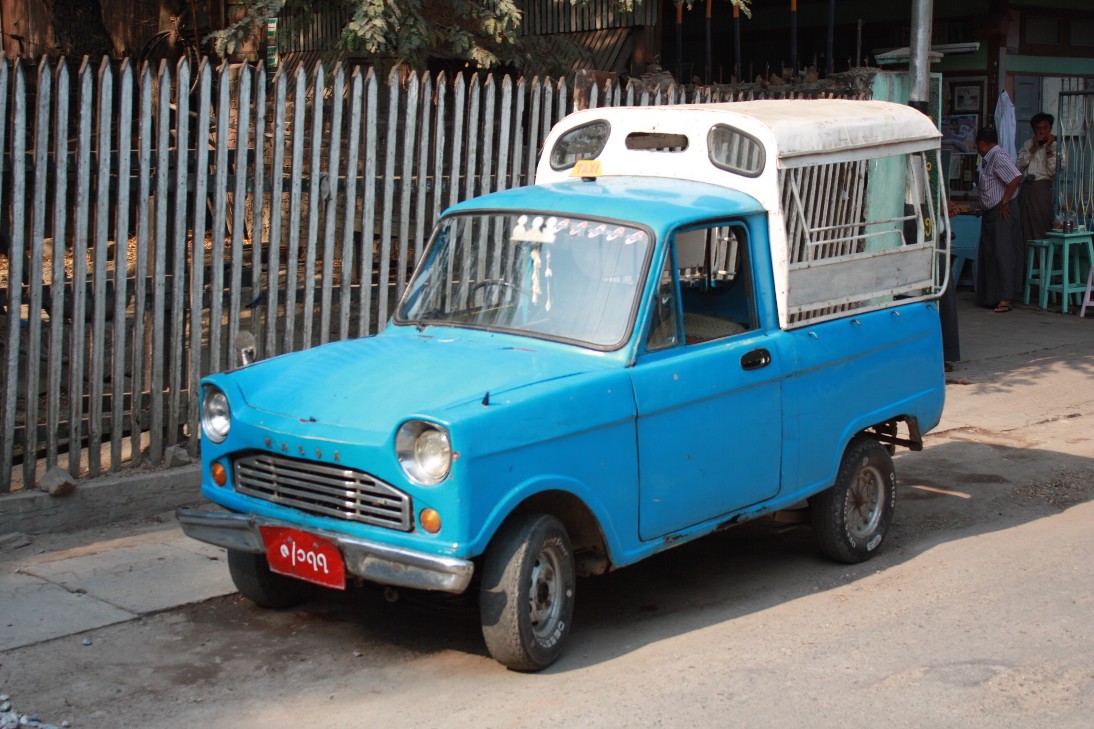 a small blue truck is parked in front of a fence