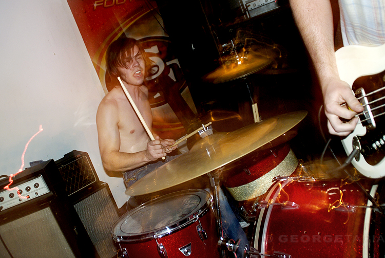 a shirtless drummer smiles while playing the drums