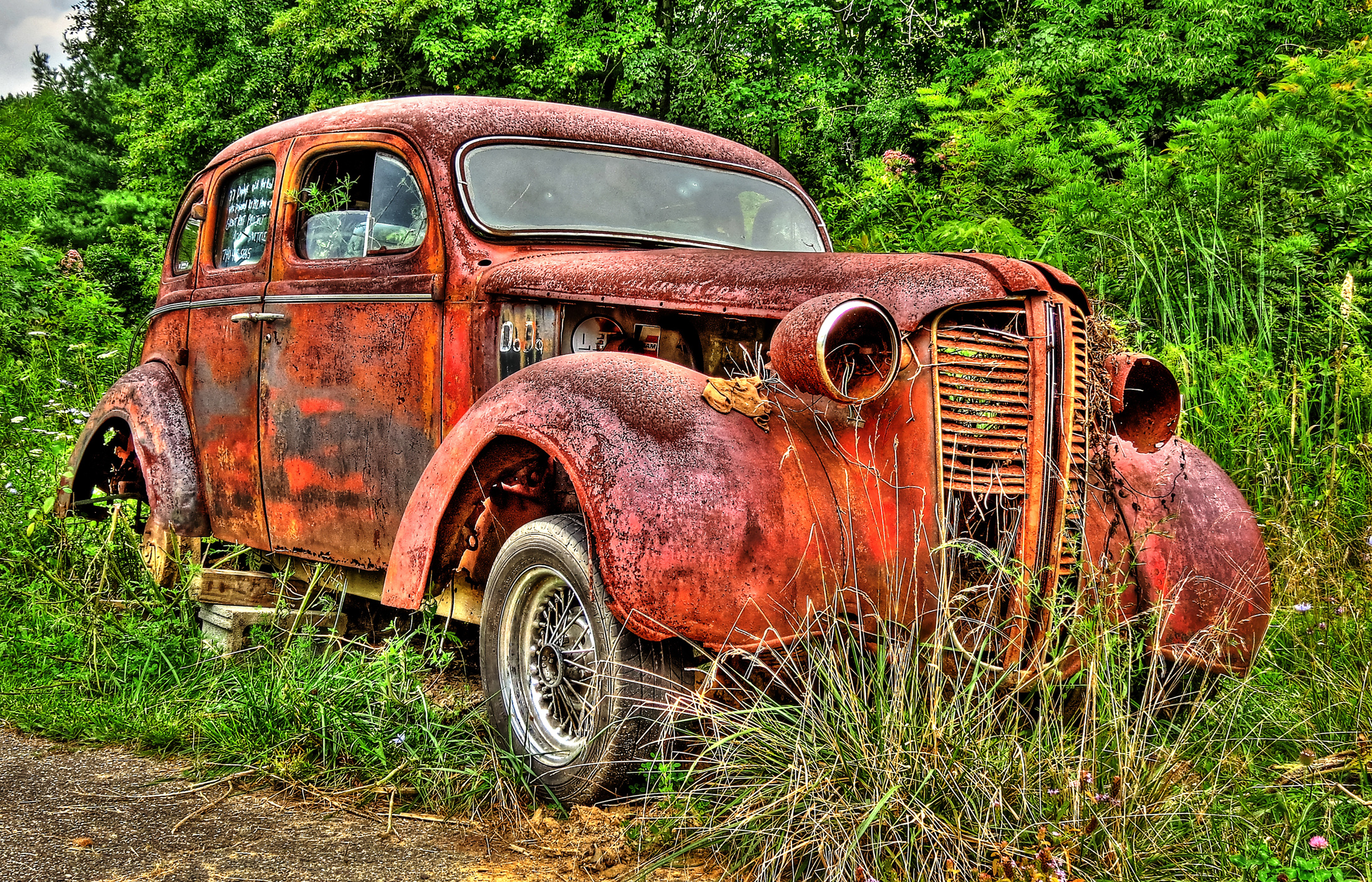 an old rusty rusted car parked in the middle of the woods