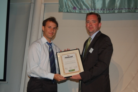 two men standing in front of a microphone holding up a certificate