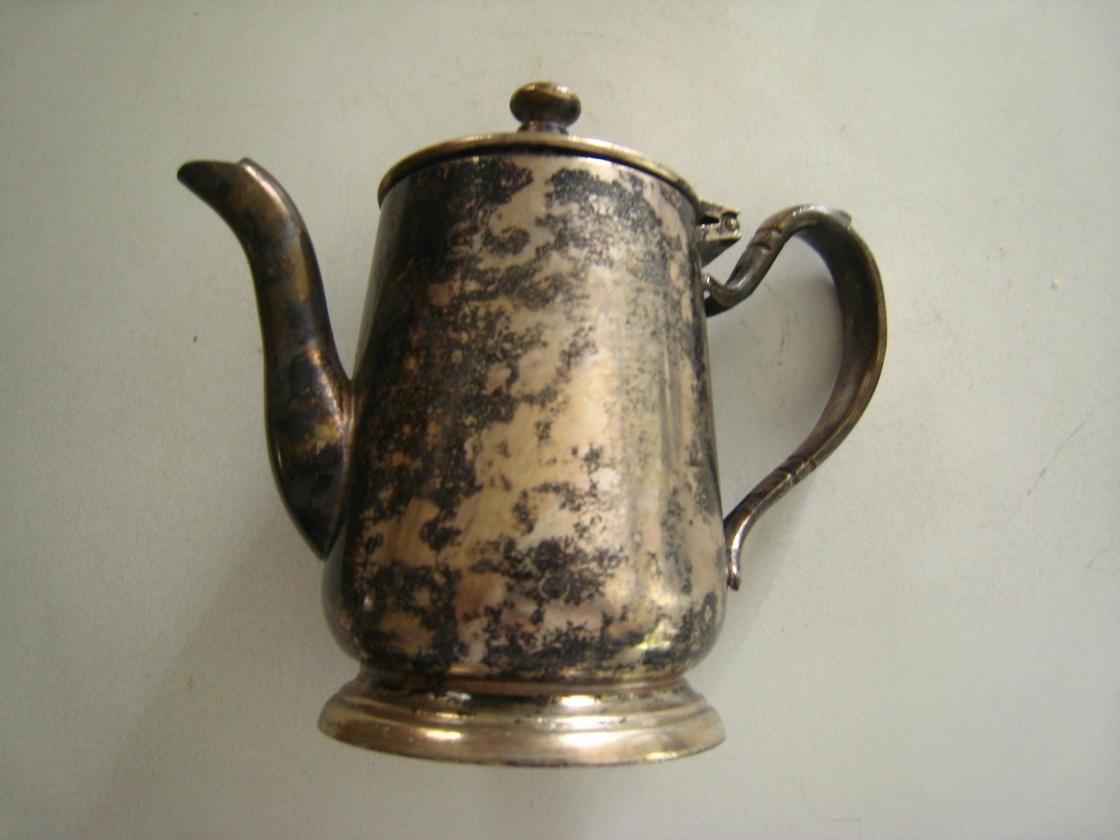 an antique silver coffee pot on display against the wall