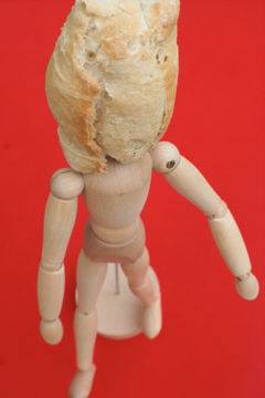 an unfinished doll with a bread bun strapped to its head