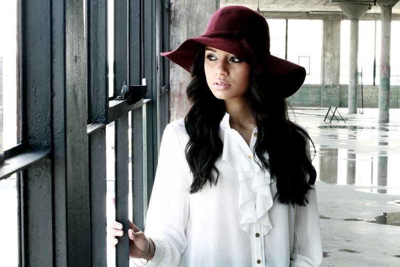 a woman with black hair standing in front of a window wearing a maroon hat