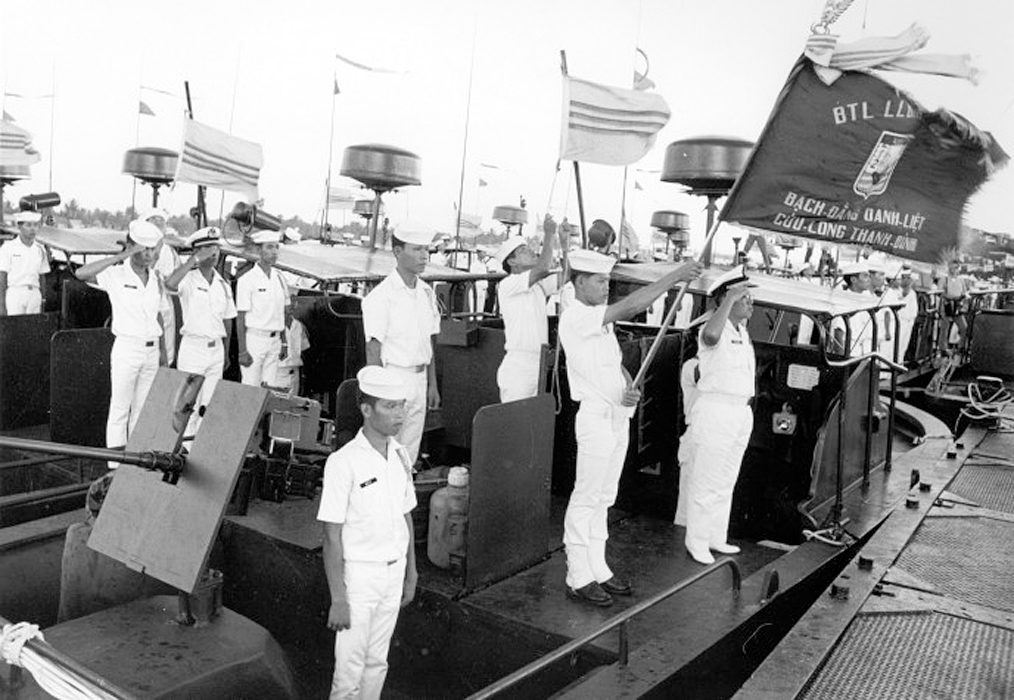 two men in white uniforms waving american flags while standing in front of a boat