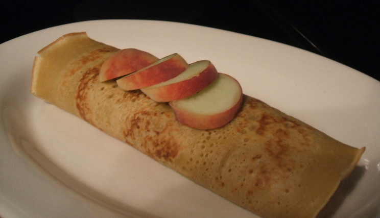 a plate topped with fruit filled crepe with sliced apples on top