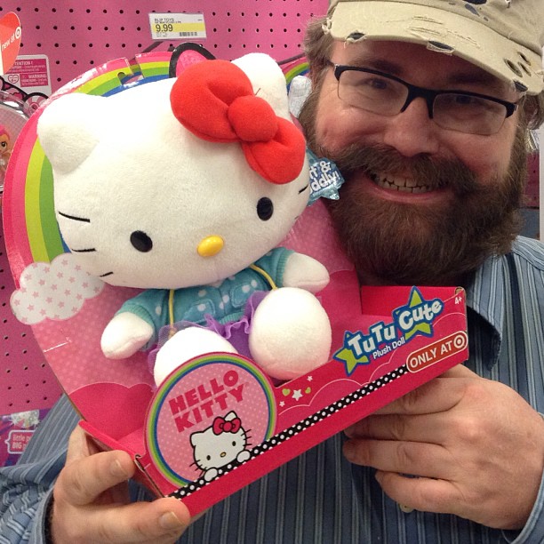 man with glasses holding a hello kitty soft toy