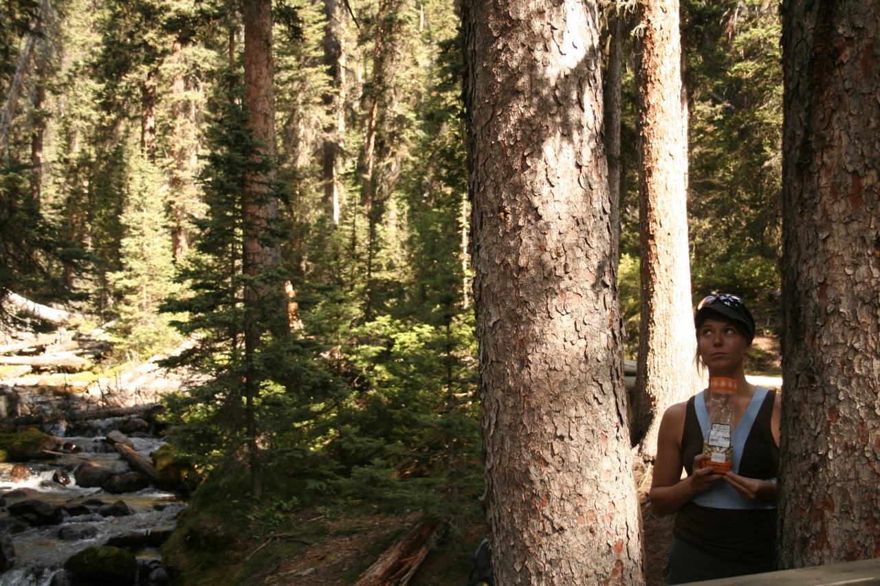 woman standing in the shade with trees and a mountain river in the background