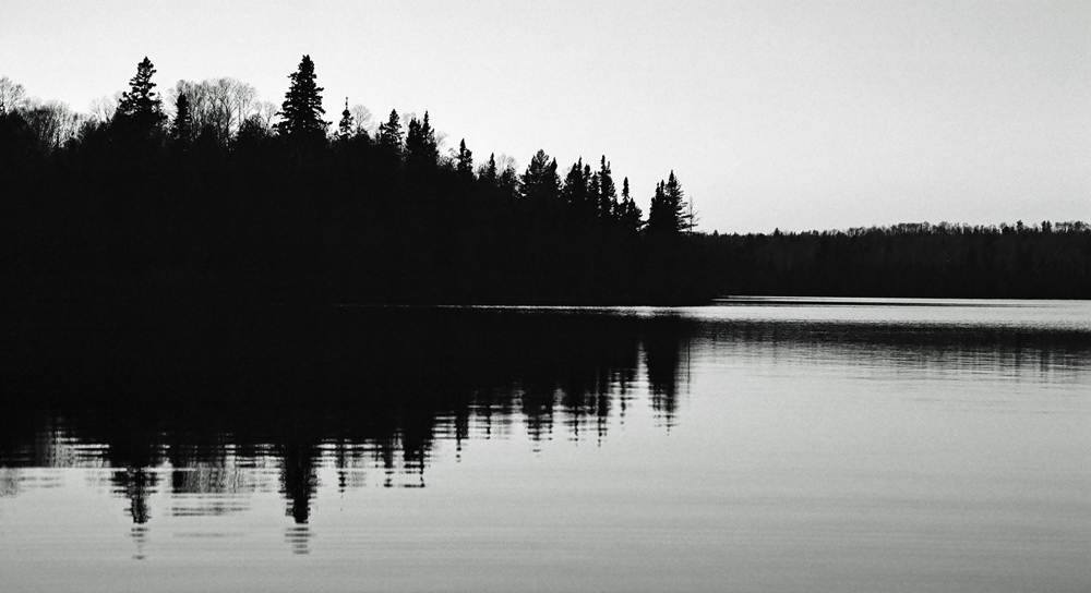trees reflect on a still lake in the early afternoon
