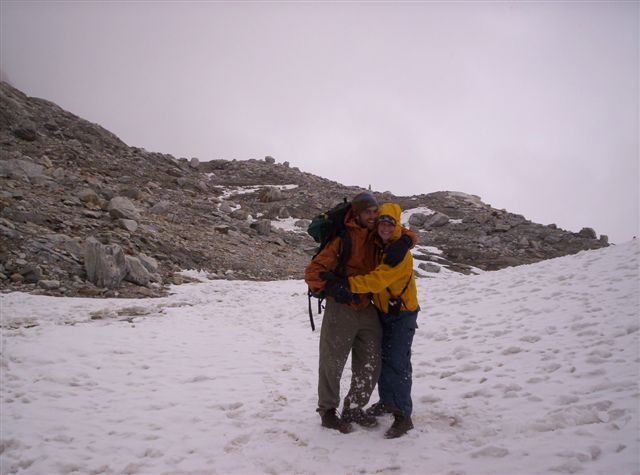 two people stand in the snow by rocks