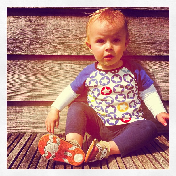 baby in blue shirt with orange shoes sitting on a wooden bench
