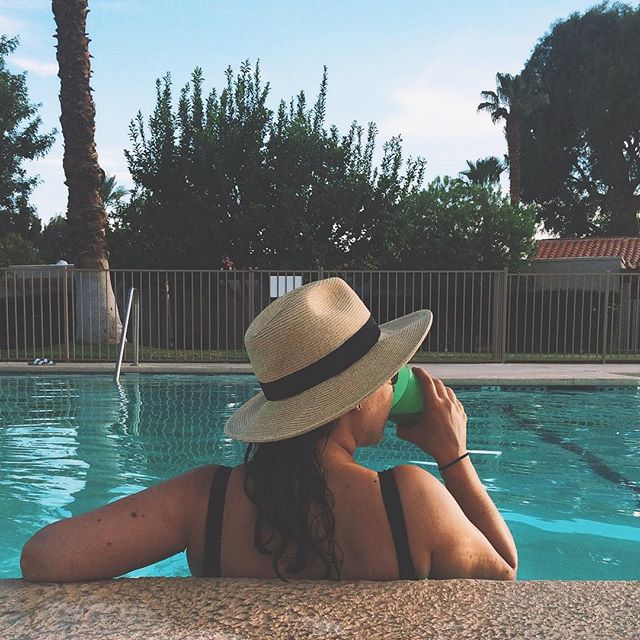 a woman sitting by a pool drinking from a cup