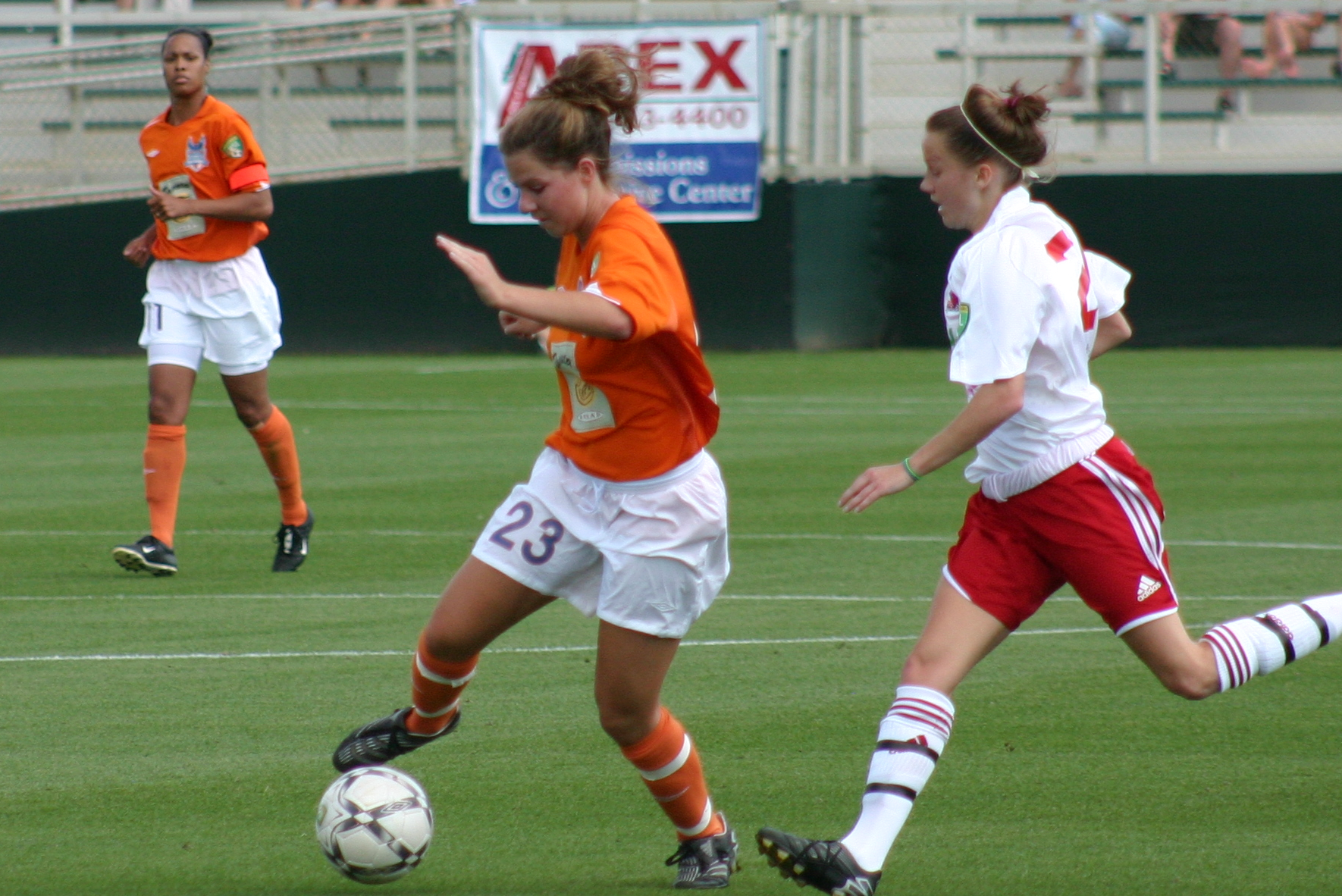 two girls playing soccer as one woman attempts to block the ball