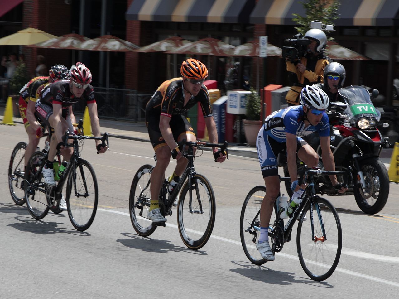 cyclists ride down the street as pedestrians watch