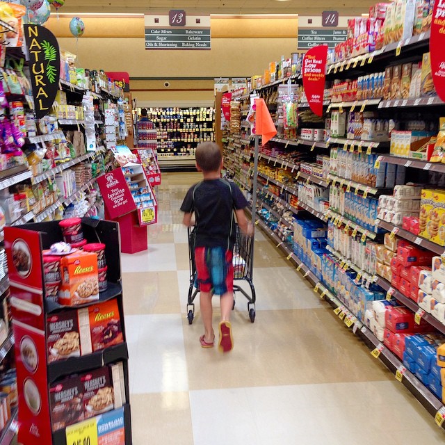 a boy hing a shopping cart through a grocery aisle