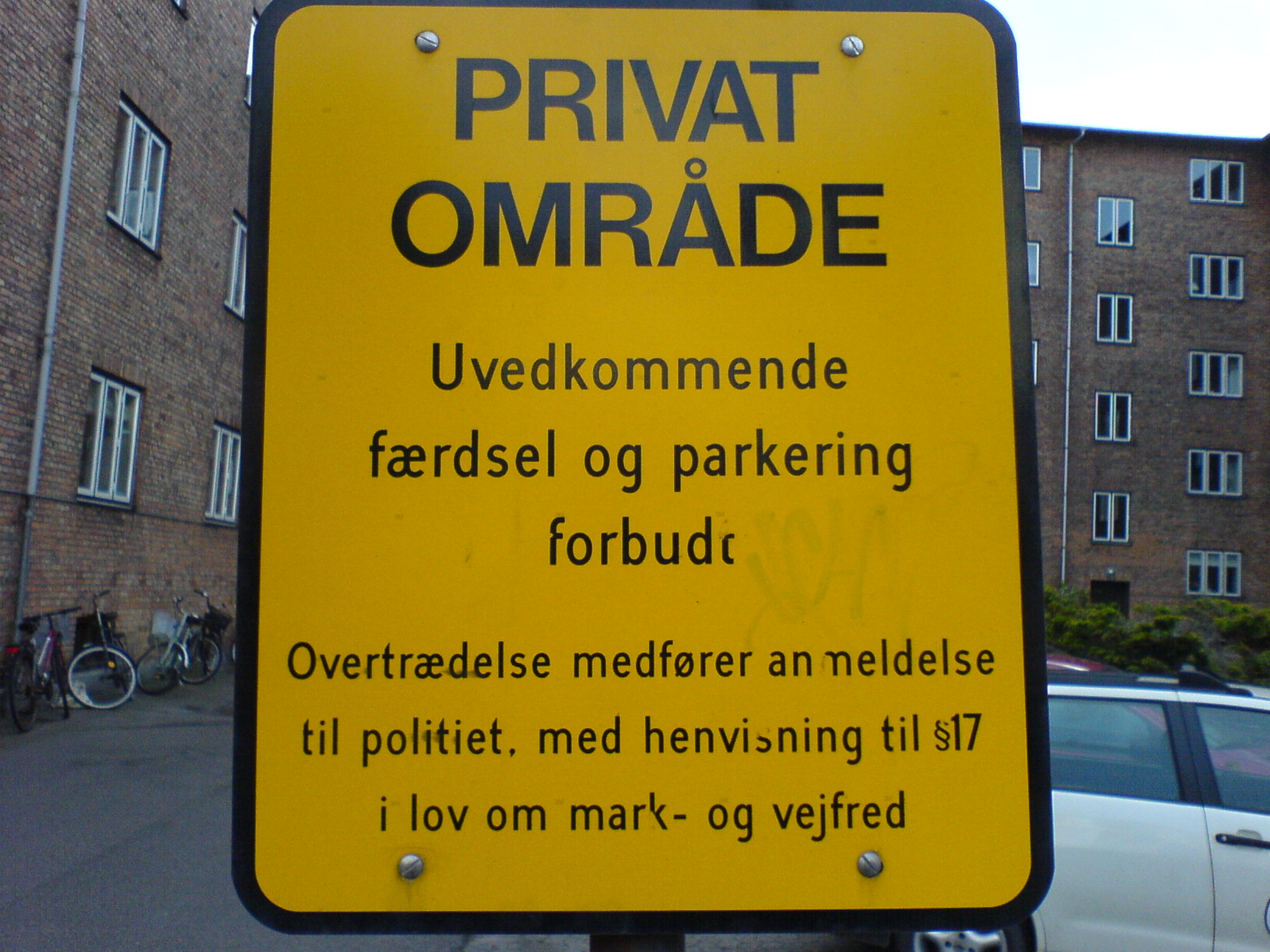a yellow sign warning of private parking with people walking around