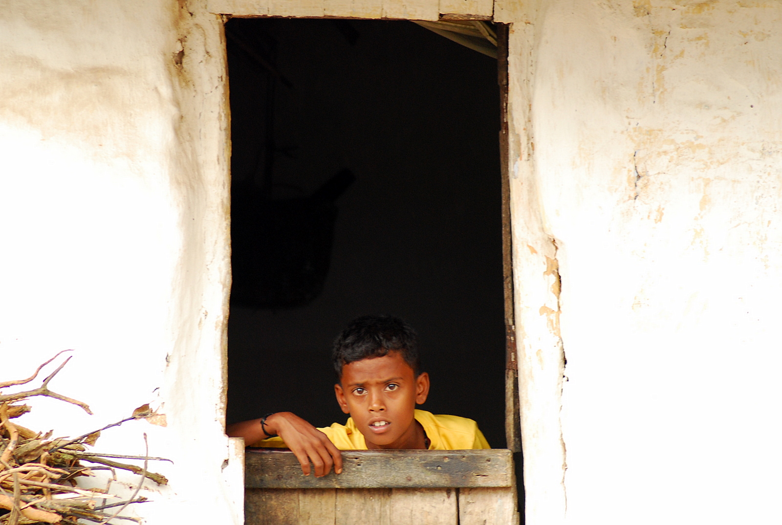 a boy wearing a yellow shirt looks out a window at the camera