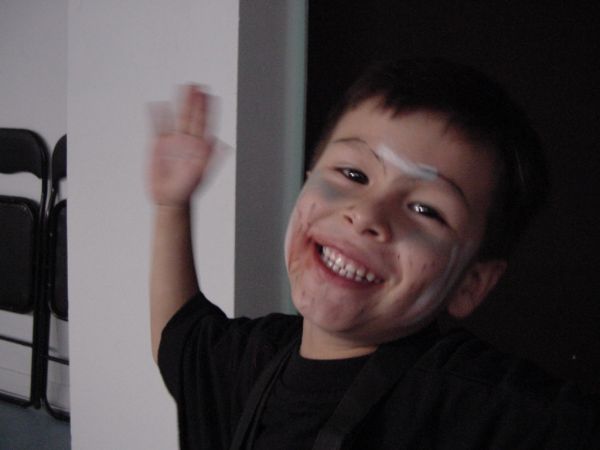 a boy holds his hand up as he smiles in the background