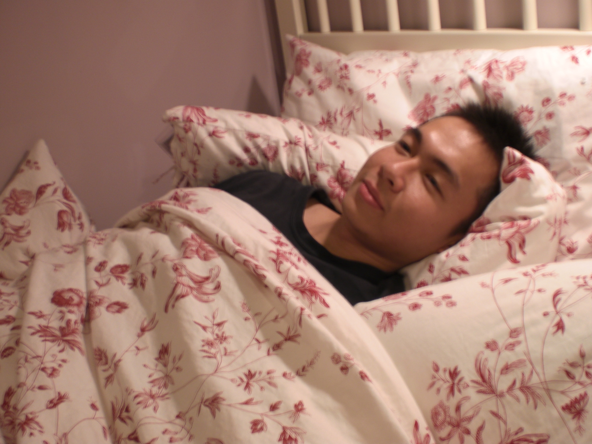 an asian man hiding in bed under a blanket