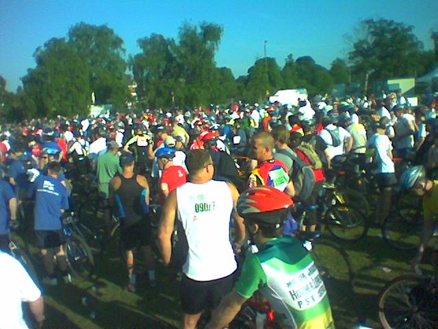 many people stand and bike while others walk in the park