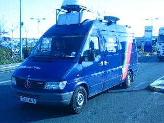 a blue van with a satellite top sitting in the middle of the road