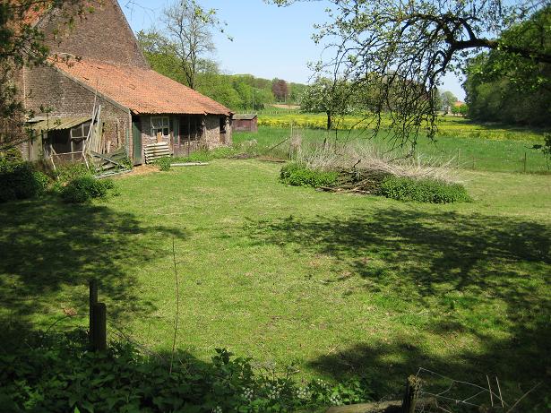 an old barn and its garden next to a green field