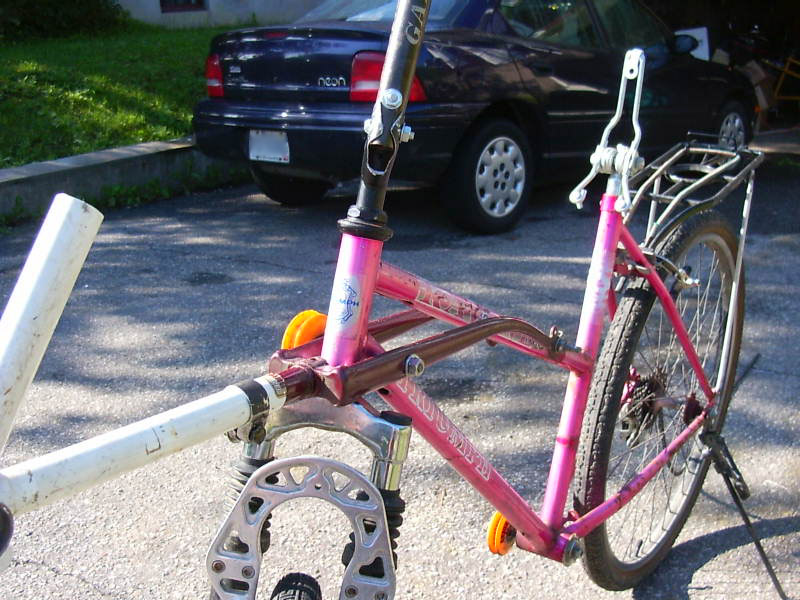 a pink bicycle is leaning against the front end of a white pole