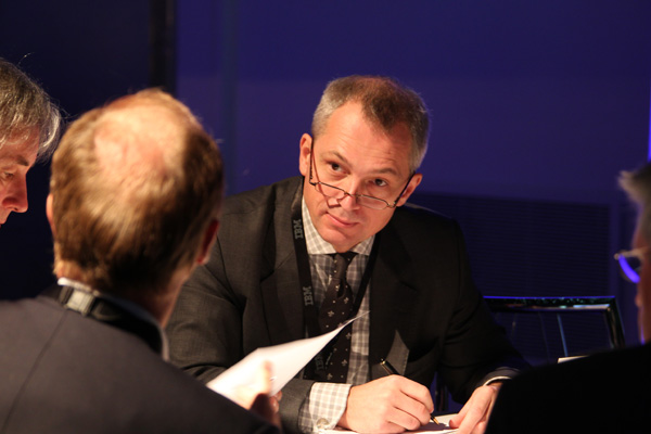 a man signing papers during an event while two others look on