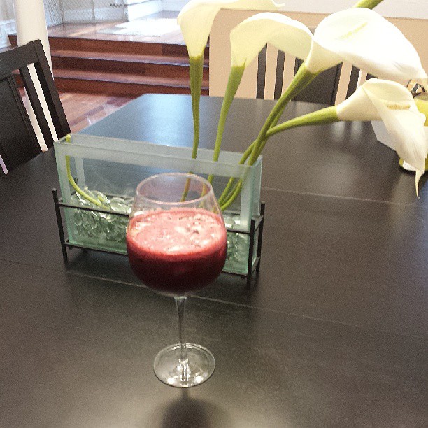 a table that has a wine glass with a liquid in it and flowers on top