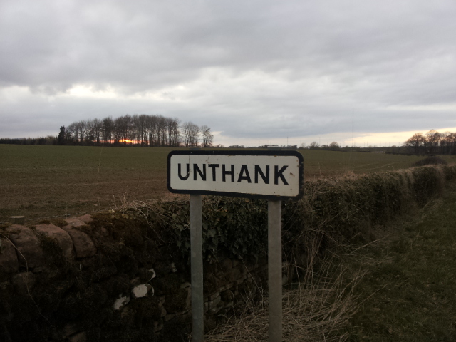 a white sign that reads unthank next to some bushes