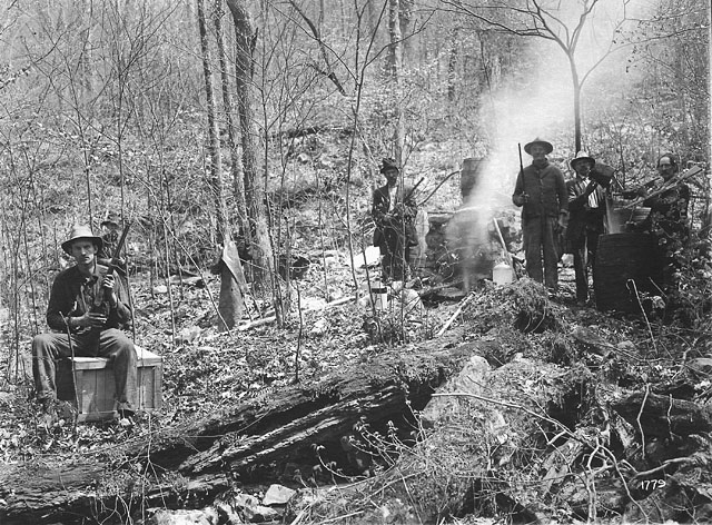 a group of men are sitting by the fire in a forest