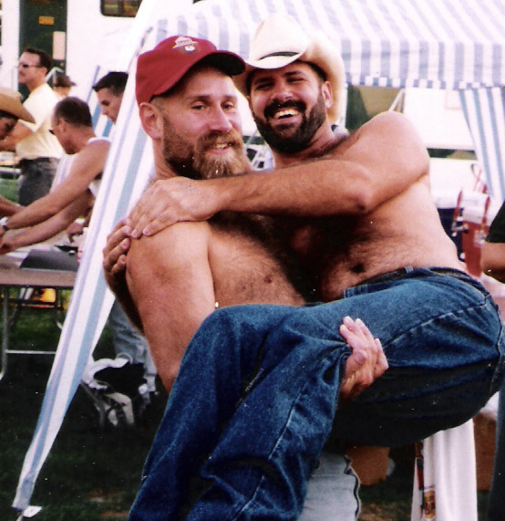 two men sitting down hugging each other in front of a tent