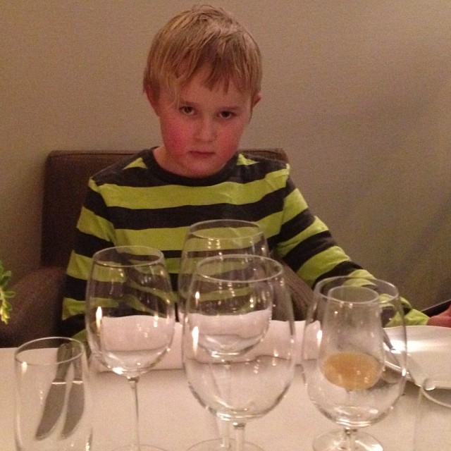 a small boy sitting at a table with some wine glasses