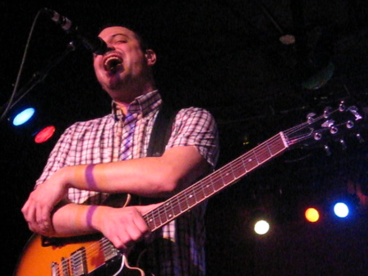 man playing guitar on stage with microphone and spotlights