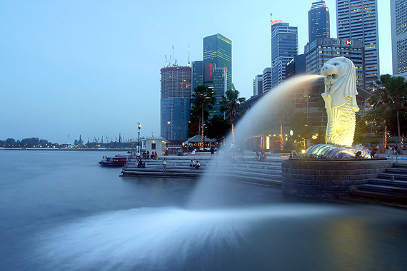 an open fountain that has a statue behind it in front of a group of boats