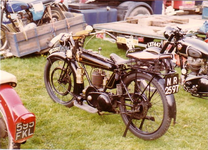 an old fashion motorcycle parked on grass in front of other motorcycles