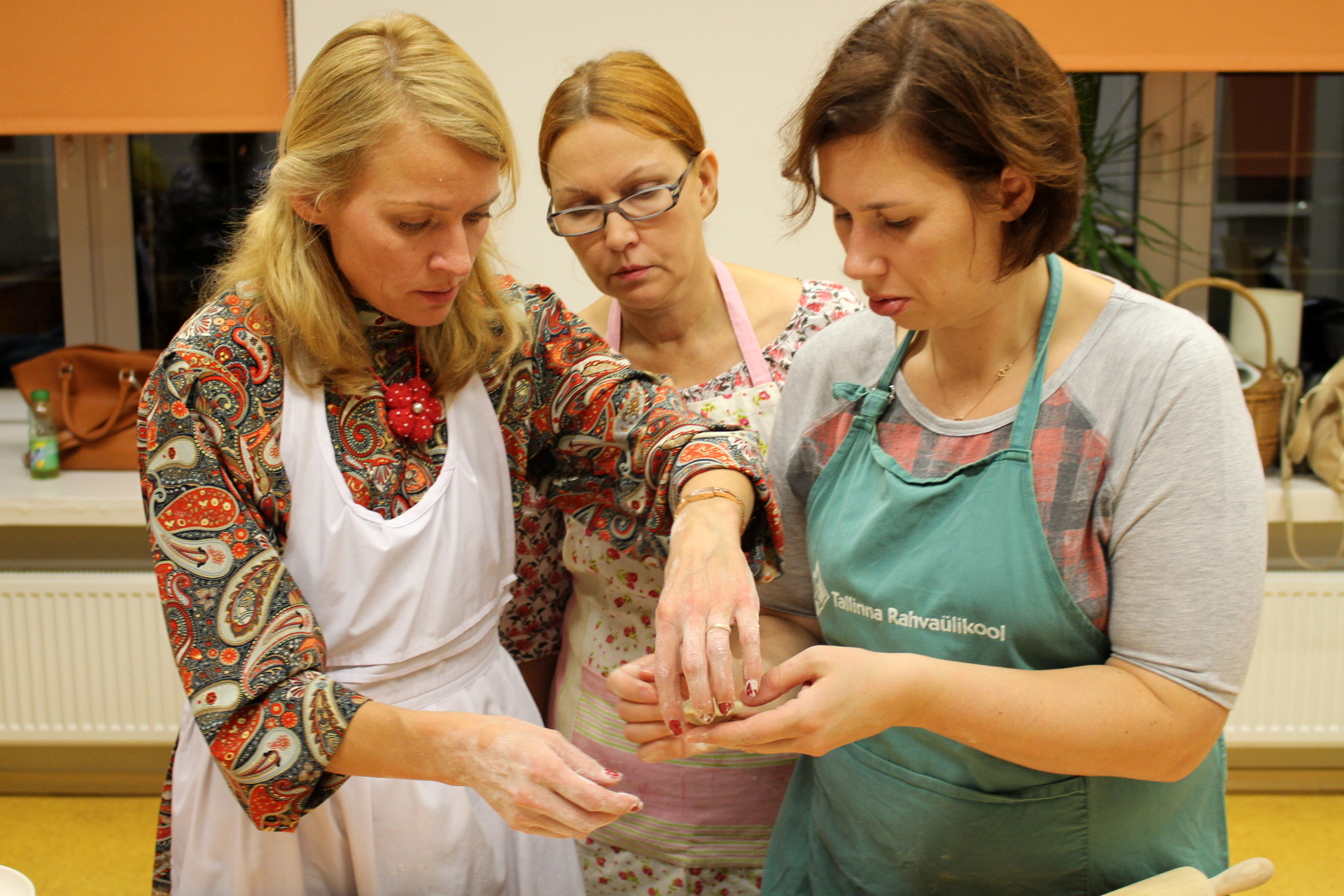 three women in aprons and ties standing over a table