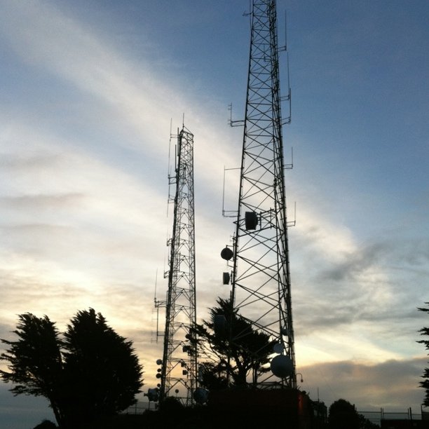 three telephone towers are silhouetted against a blue cloudy sky