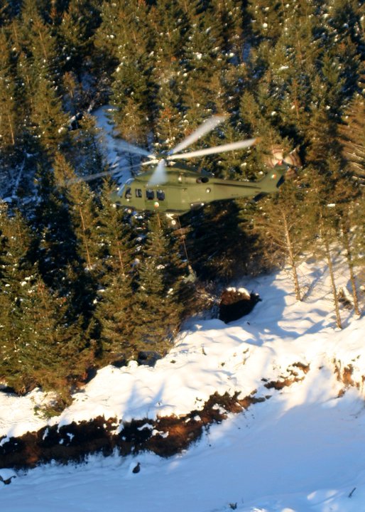 a helicopter flying over the snowy ground in front of trees