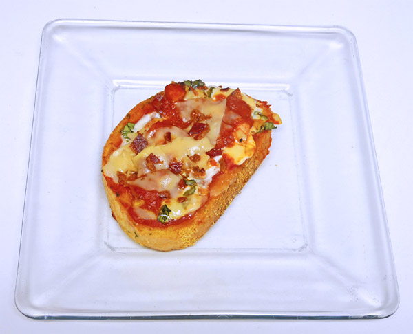 a rectangular plastic tray has a tiny pastry dish topped with cheese, sauce and other toppings