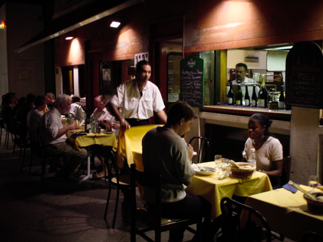 several men sit at tables while another cooks orders